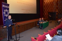 alt= "Policjant moderujący debatę przedstawia program."