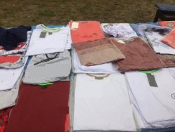 alt="Na  zdjęciu widoczny stragan z poukładanymi równo koszulkami(t-shirtami)."