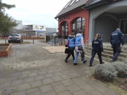 alt=&quot; Policjant oraz policjantka poruszają się w kierunku placówki usługowej wraz z dwoma pracownicami sanepidu.&quot;