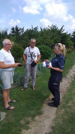 alt=&quot; Policjantka rozmawia z dwoma mężczyznami, działkowcami na terenie ogródków działkowych.&quot;