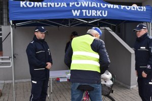 alt=&quot;Policjanci w trakcie przekazywania kamizelek odblaskowych rowerzystom przed budynkiem KPP w Turku.&quot;