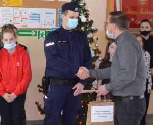 alt=&quot; Funkcjonariusz z Komendy Powiatowej Policji odbiera z rąk Dyrektora Szkoły Podstawowej w Chełmnie przygotowane podziękowania.&quot;