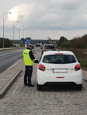 alt=&quot;Policjant podczas kontroli pojazdu marki Peugeot koloru białego.&quot;
